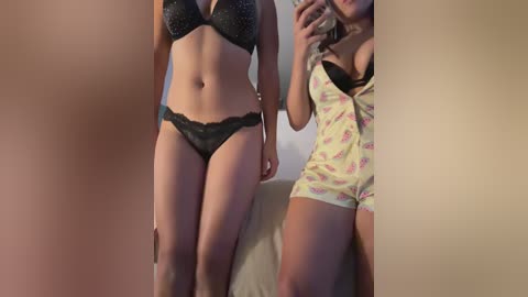 A video of two women in matching black lace lingerie, posing in front of a mirror, with a light-colored background.