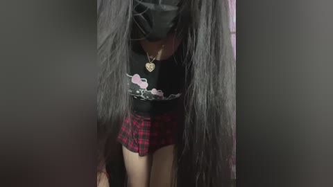 Video of a young Asian woman with long black hair, wearing a black shirt, pink floral skirt, and black thigh-high stockings, bending forward.