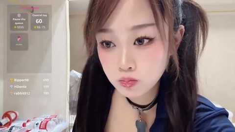 Video of an Asian woman with fair skin, wearing black hair in pigtails, heavy makeup, and a black choker, looking pensive indoors.