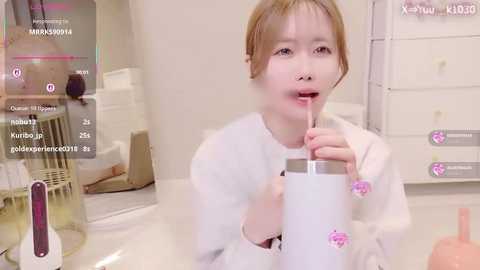 Video of a young Asian woman with light skin, short brown hair, wearing a white lab coat, sipping from a frosted pink Starbucks cup, in a sterile laboratory setting.