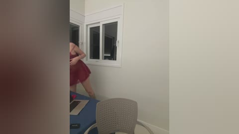 A video showing a woman in a red dress standing near a blue pool table in a minimalist room with white walls and a window.