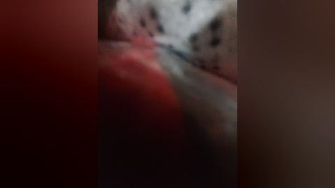 A blurred video featuring a person with dark skin, possibly of African descent, lying on a bed with red sheets, wearing a white shirt. The image is out of focus, making details indistinct.