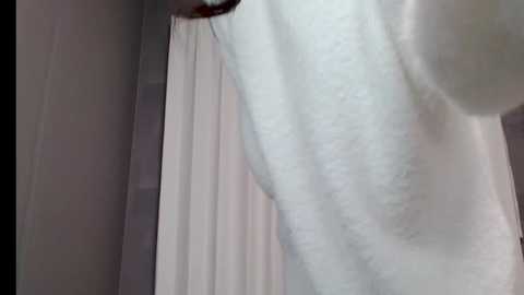 A close-up video of a person in a white towel standing in a shower with a beige curtain and gray tiled walls.