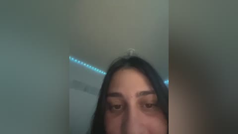 A blurred video of a young woman with long dark hair, her face partially obscured by the camera's focus. The background features a dimly lit room with a blue LED strip light.