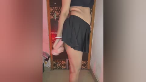 Video of a light-skinned woman in black athletic shorts and sports bra, standing in a dimly lit room with beige walls and a patterned tile floor. She's adjusting her right sock, with a small dog visible in the background.