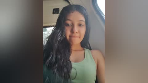 Media: Video of a young Asian woman with long black hair, wearing a light green sleeveless top, seated in a car.