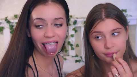 Video of two young women, one with long brown hair and braces, sticking out her tongue, the other with long brown hair, smiling, both wearing casual outfits.