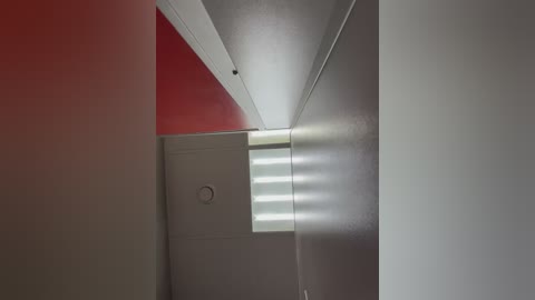 Video of a minimalist interior corner featuring a bright, white ceiling and walls. A small, round ventilation hole is visible on the ceiling. A red wall contrasts with the white. The room's lighting is soft and natural.