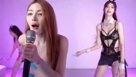 Video of two Asian women in a studio, one in a strapless turquoise top, singing into a microphone, the other in a black lace bodysuit, smiling.