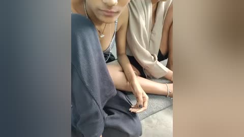 Video of two women sitting closely, one in a blue dress, the other in a beige top, legs crossed, with blurred faces.