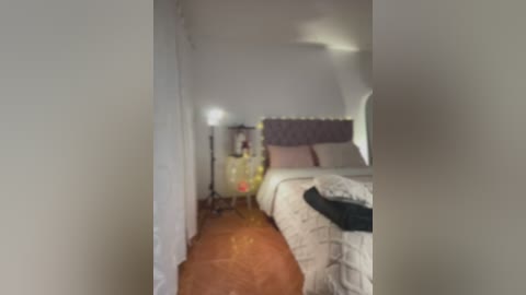 Media: A blurry video of a dimly lit bedroom with a bed, wooden floor, white walls, and a chair with a lamp on the left.