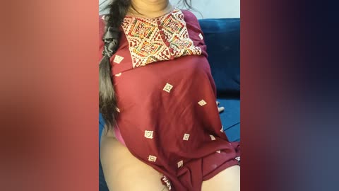 A video of a woman wearing a maroon saree with intricate white embroidery, partially exposing her lower body, against a dark blue background.