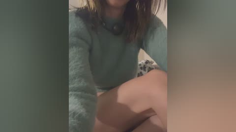 Video of a woman with light skin and brown hair, wearing a fuzzy, light gray sweater, sitting cross-legged on a bed with leopard print sheets.