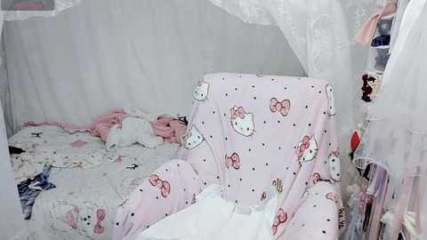 Video of a cluttered, girly bedroom with a white canopy bed covered in Hello Kitty-themed bedding, featuring pastel pink and white patterns, and various toys and stuffed animals scattered around.