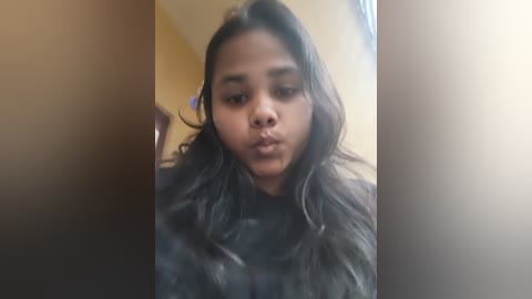 Video of a young Asian woman with long black hair and dark eyes, wearing a black fur-like jacket, standing indoors with a blurred background.