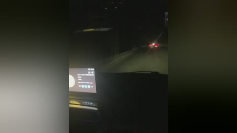 A dimly-lit, grainy video captures a nighttime scene from inside a moving car, featuring a bright red taillight ahead and a smartphone screen displaying a music app.