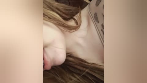 A video of a close-up view of a young woman's bare chest and face. Her skin is fair, and her long, light brown hair partially covers her left breast. The background is blurred, focusing on her intimate body parts.