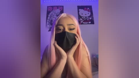 Media: Video of a young woman with long, pastel pink hair, wearing a black face mask, holding her hands to her face. Background features purple lighting, two My Melody posters, and a darkened room.