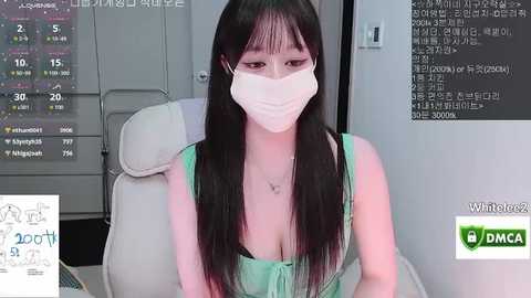 Media: Video of an Asian woman with long black hair, wearing a green sleeveless top and a white face mask, seated in a white leather chair, in a modern office setting with a monitor and Korean text.