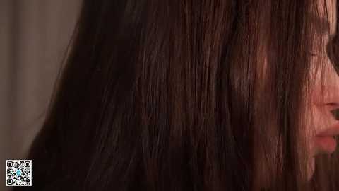 A close-up video of a woman's dark brown, straight hair, with fine strands visible. Her face is partially visible, showing a gentle smile. The background is blurred, focusing on the texture and color of the hair.