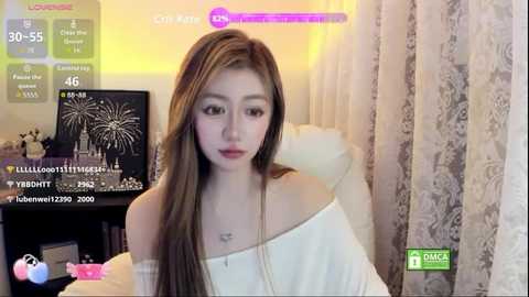 Media: Video of an Asian woman with long brown hair, wearing an off-the-shoulder white top, seated in a cozy room with curtains and a TV showing fireworks.