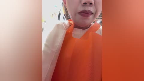 Video of a person wearing an orange apron over a white shirt, with light skin and a hint of makeup. Background shows a blurred kitchen with white walls and a countertop.