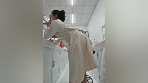 A video of an Asian woman in a white lab coat and glasses, leaning over a lab counter, examining a petri dish.