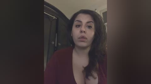 Media: A video of a woman with long, dark hair, wearing a maroon top, standing in a dimly lit hallway.