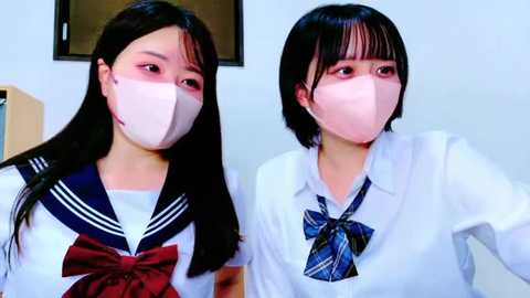 Video of two young Asian women in matching white school uniforms with blue plaid ties, wearing face masks, looking side by side.