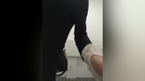 Video of a person's legs in black pants, walking through a narrow, dimly lit corridor with white walls and a black door on the left.