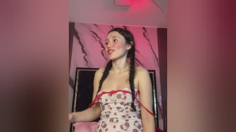 Media: Video of a young woman with pale skin, dark braided hair, and a white dress with red floral patterns, standing against a pink marble wall with red lighting.