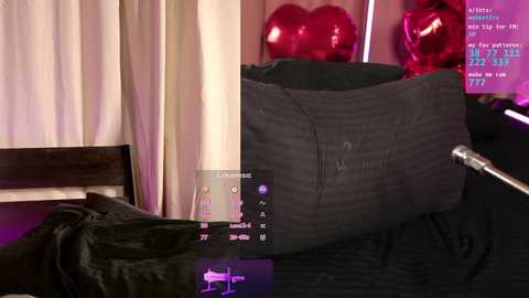 Video of a plush, striped black and white bear, surrounded by red heart balloons, on a dark bed with white sheets, in a dimly lit room.