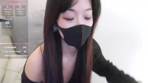 Video of an Asian woman with long black hair, wearing a black mask, black top, and closed eyes, taken indoors with a blurred background.