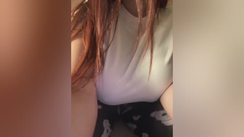 Video of a woman with long, auburn hair, wearing a white sleeveless top and black pants with a skull pattern, captured from a slightly elevated angle.