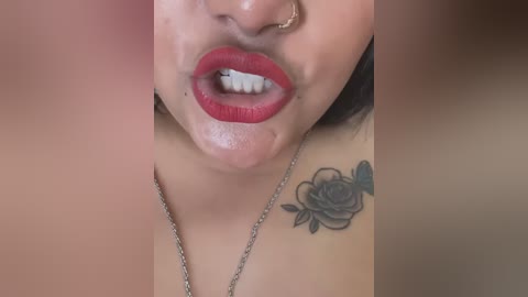Video of a close-up of a smiling woman with medium skin tone, red lipstick, and a small rose tattoo on her shoulder. She wears a gold nose ring and a delicate necklace.