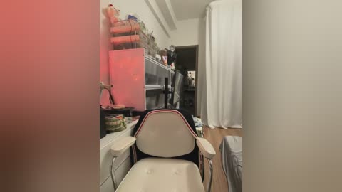 A video of a cluttered, narrow hallway with a white chair, a sink, and a partially open door revealing a messy bedroom.