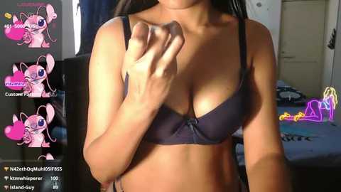 A video of a woman in a dark bra, taken from a low angle, showing her cleavage. Background includes a bed with a purple neon light and a door.