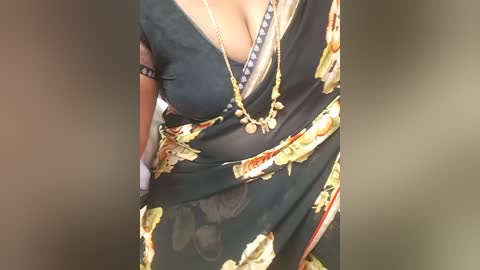 A video of a woman in a black floral dress, showcasing a plunging neckline revealing ample cleavage, adorned with multiple necklaces and bracelets. The background is blurred, focusing on her torso.