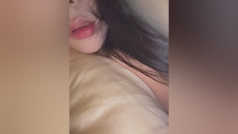 Video of a close-up of a woman's partially visible face and shoulders, with fair skin, pink lips, and long dark hair, lying on a beige pillow, creating a soft, intimate atmosphere.