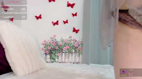 Video of a bedroom with a plush white bed, a bouquet of pink roses in a vase, and red butterflies on a white wall.