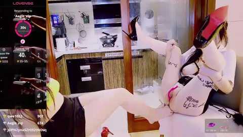 Video of a woman in a white and red BDSM outfit, legs spread, on a desk, surrounded by kitchen appliances and a computer screen showing a GPS route.