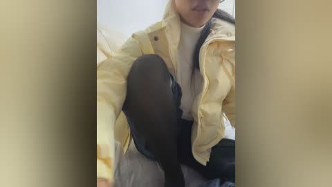 A video of a person wearing a yellow jacket over a white shirt, sitting on a black motorcycle. The background is blurry, showing indoor lighting. The image is cropped to focus on the torso and legs.