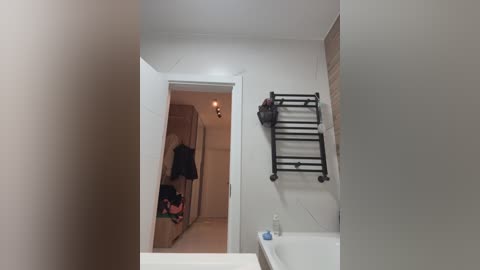 Media: Video of a modern bathroom with a white tiled wall, black towel rack, and a partially open closet door showing clothes hanging inside.