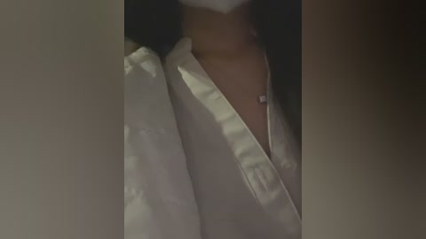 Media: A video of a person's upper body, wearing a white, slightly unbuttoned shirt, casting a shadow on a dark background. The image is dimly lit, creating a moody atmosphere.