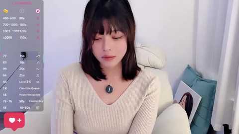 Video of a young Asian woman with straight, shoulder-length black hair, wearing a cream ribbed sweater, sitting on a white leather couch, eyes closed, reading a book.