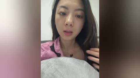 Video of an East Asian woman with long black hair, light skin, and a pink top, smiling with parted lips, blurred background.