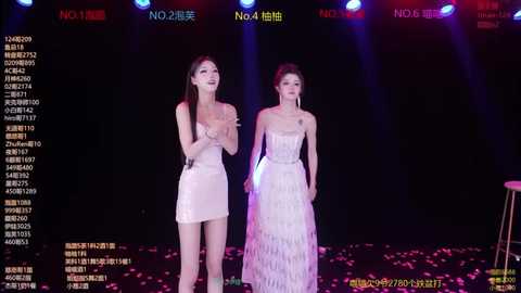 Video of two East Asian women, one in a strapless, pink sequined dress, the other in a white, beaded gown, standing on a stage with colorful lights and Chinese text on the screen background.