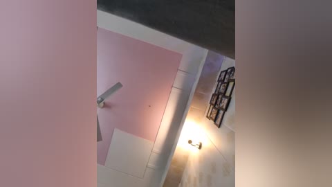 A video showing a narrow, white-tiled hallway with a pink wall on the left and a dark metal railing on the right. A small, white light bulb emits a soft glow at the end of the hallway.