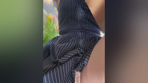 Video of a woman in a black pinstripe dress, bent over, showing a glimpse of her panties, against a blurred green and blue background.