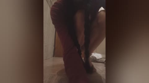 A blurry video of a person in a dark outfit bending over, taken in a dimly lit room with tiled flooring and beige walls.